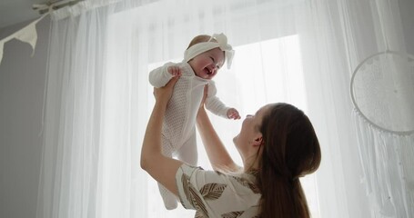 mother and child have fun at home together. young beautiful mom throws her adorable newborn baby up 