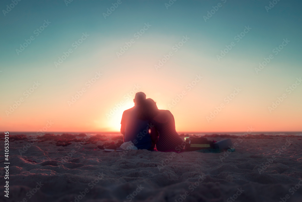 Pareja de enamorados sentados en la playa mirando el amanecer - obrazy, fototapety, plakaty 