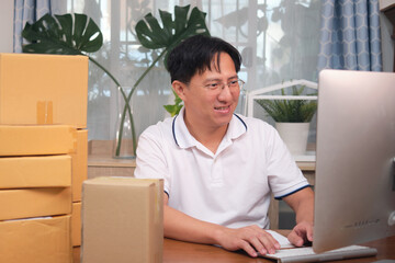 Asian happy smiling business man entrepreneur using computer looking at screen work at home online shopping with postal box prepare parcel delivery, Small business owner at home office concept