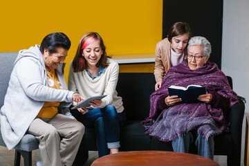 Wall Mural - Latin granddaughter and mexican grandmother reading a book and tablet in Mexico city