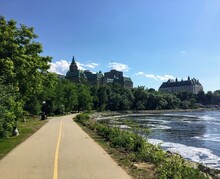 A Beautiful Bike And Walking Path Along The Ottawa River On A Sunny Summer Day With Blue Sky.  The Supreme Court Of Canada Is In The Distance, In Ottawa, Ontario, Canada.