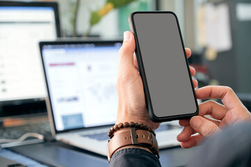 Closeup image of man hands holding blank screen smartphone while sitting at office desk.