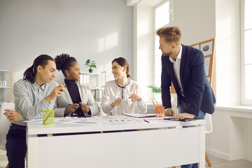 Happy diverse company workers sitting at office desk and discussing project in group meeting. Team of people talking, analyzing financial growth charts and graphs and developing new business strategy