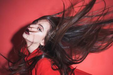 Wall Mural - Crazy girl waving her hair. Woman with stylish makeup and long hair posing in total red outfit. Fashion concept. Girl on mysterious face in red formal jacket, red background.