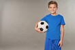 © Friends Stock - Cheerful boy with soccer ball standing against gray background