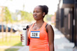 © Syda Productions - fitness, sport and healthy lifestyle concept - happy smiling young african american woman or marathon runner drinking water from bottle outdoors