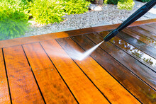 Cleaning The Terrace With A Pressure Washer - High-pressure Cleaner On The Wooden Surface Of The Terrace - Very Shallow Depth Of Field - Sharpness On The Terrace Board Under A Stream Of Water