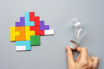 Hand holding lightbulb with colorful wood puzzle piece on gray background. New Idea, Creative, Innovation, Imagination, inspiration, Solution, Strategy and Logic concept