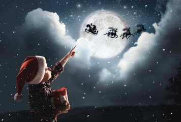 Sticker - Cute little boy looking at Santa Claus with reindeers in sky on full moon night. Christmas holiday