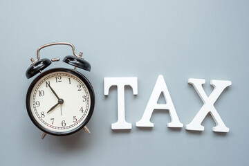 TAX text and alarm clock on gray background. investment and time to tax concepts