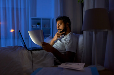 Sticker - work, remote job and people concept - young indian man with laptop computer and papers working in bed at home at night