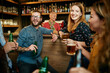 © chika_milan - Group of cheerful friends standing near bar counter, drinking beer and chatting.