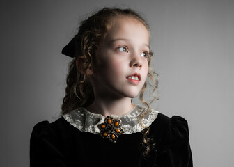 Beautiful young girl in black 1890s English Victorian 18th century child period dress with elegant white lace collar antique broach jewellery and long curly pretty hair looking away from camera