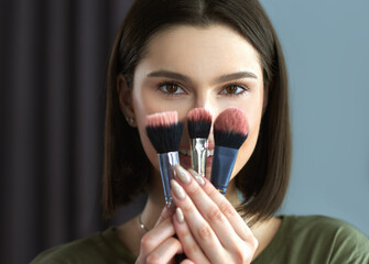 Canvas Print - Closeup of a brunette girl showing her make-up brushes. Candid portrait of a young woman makeup artist holds some brushes in her hands.