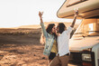 Happy beautiful hipster couple toasting with wine at sunset, standing near old camper. Travel, nomadic, real people lifestyle and emotions concept.