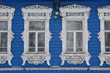 Ornamental windows with carved frames on vintage blue wooden rural house in Maydakovo village, Ivanovo region, Russia. Building facade. Russian traditional national folk style in wooden architecture