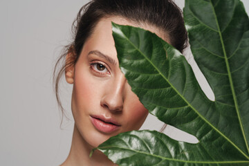 Beautiful half-naked woman posing with green leaf on camera