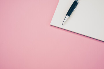 Wall Mural - Top view closeup of a pen placed on an open notebook isolated on a pink background