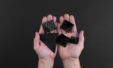 black geometric pyramids in hand isolated on black background