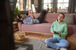 © AnnaStills - Teenage girl sitting on the floor playing video game with boy lying on sofa playing on the phone in the room