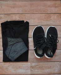 Woman's sport clothes. Sport bra, t-shirt and black shoes. Everything on a wooden background.