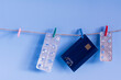 Debit card and empty pills blisters hanging with plastic clothespin twine on blue background. Concept of medicine and sale of drugs.