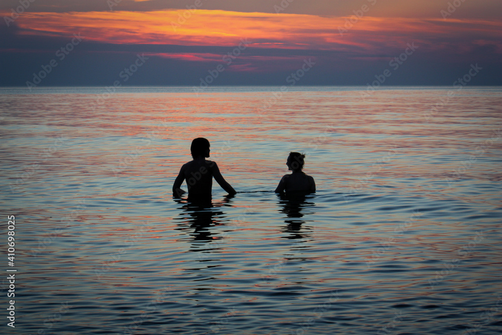 zakochana para chłopak i dziewczyna wchodzą do wody przy zachodzie słońca na plaży nad morzem bałtyckim - obrazy, fototapety, plakaty 
