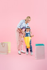 full length of happy mother and smiling daughter looking at shopping bag on pink