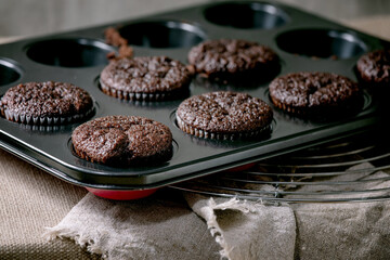 Fresh baked homemade chocolate cupcakes muffins in form for cooking standing on kitchen table with tablecloth. Home bakery