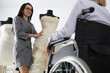 Woman consultant demonstrates wedding dress on mannequin to woman in wheelchair