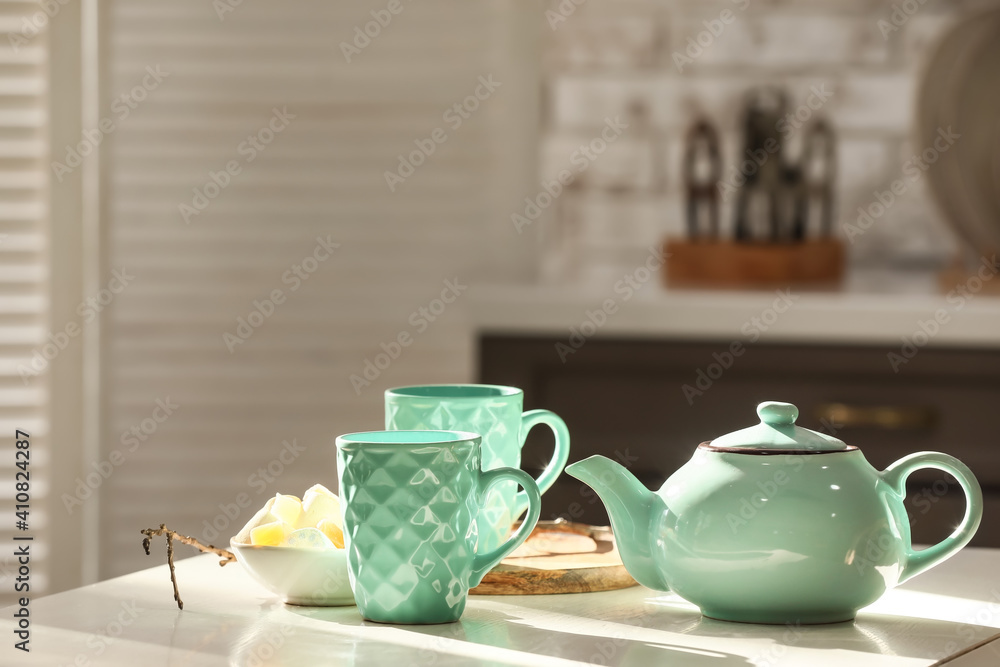 Stylish teapot and cup on light table in room