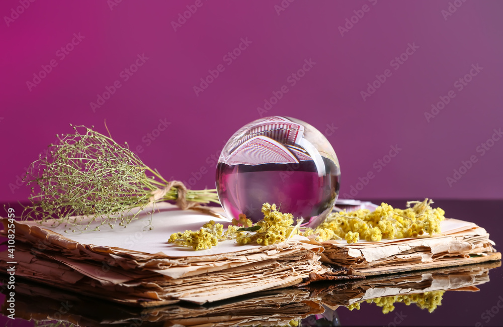 Crystal ball of fortune teller, old book and dry herbs on table