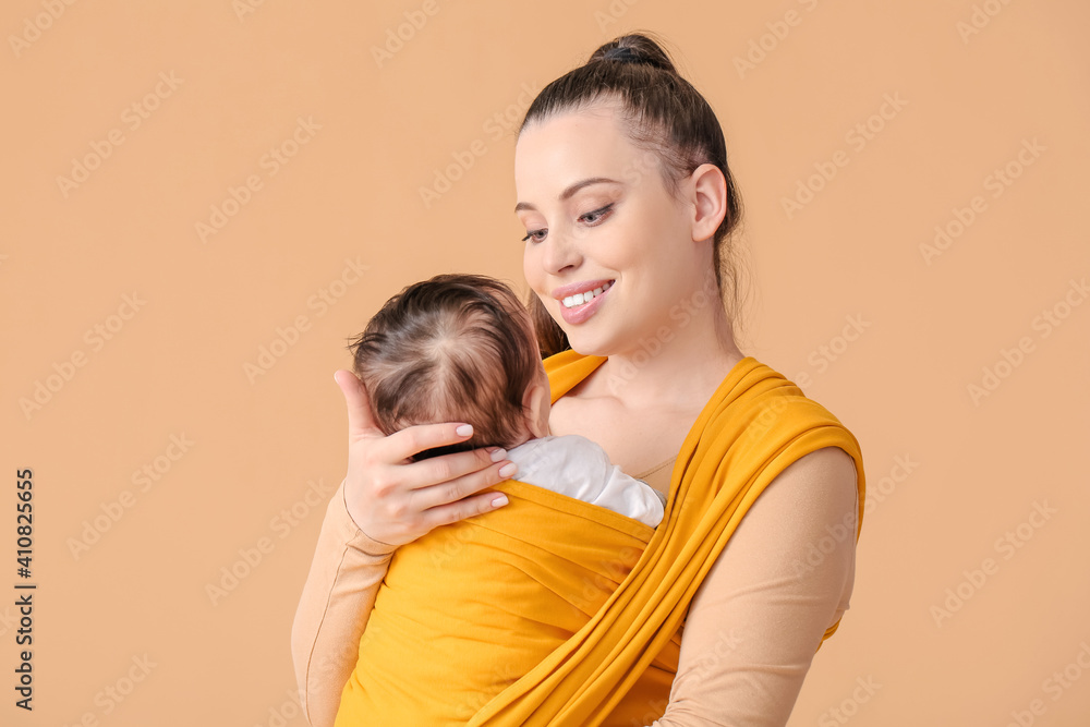Young mother with little baby in sling on light background