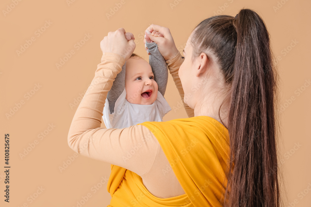 Young mother with little baby in sling on light background