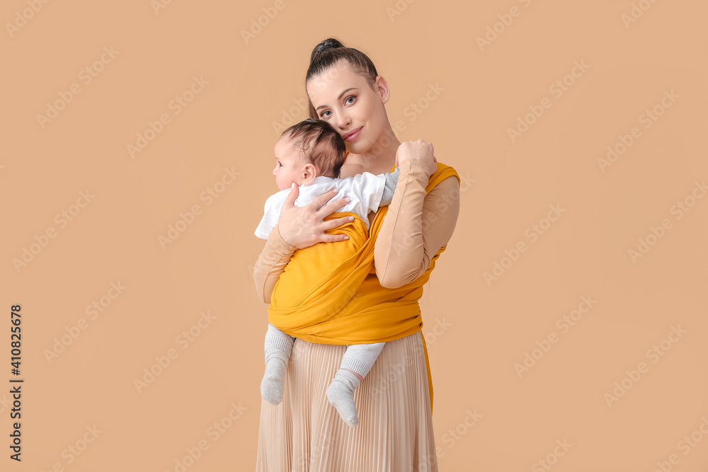 Young mother with little baby in sling on light background
