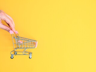 Mini cart and female hand on yellow background. The concept of shopping in stores and on the Internet. Online shopping concept