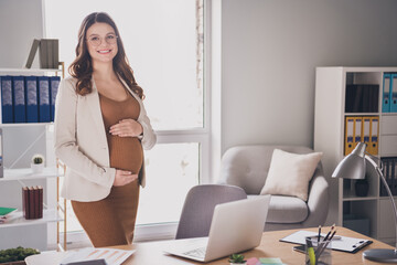 Poster - Photo of pregnant happy young woman hands hold big belly wear spectacles suit brown dress workstation office indoors