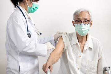 Asian doctor with syringe doing injection of vaccine,nurse vaccinating elderly in the hospital,vaccination to old senior at risk of Coronavirus infection to stimulate immunity against COVID-19 disease