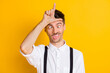 Photo portrait of comic silly ridiculous man showing looser sign abusing fooling grimacing isolated on bright yellow color background