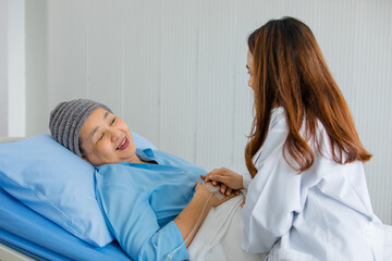 Older Asian woman patient covered the head with clothes effect from chemo treatment in cancer cure process talking to a female doctor