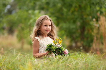 Wall Mural - Cute little girl holding wreath made of beautiful flowers in field