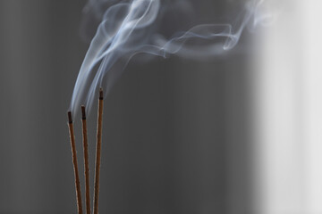 Incense sticks smoldering on blurred background, closeup. Space for text