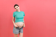 Happy Pregnant Woman In Unzipped Jeans Showing Her Naked Belly At Colorful Background With Copy Space. Baby Expecting Concept