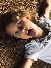 Portrait Of Girl Sticking Out Tongue While Lying On Grain