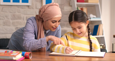 Little girl doing homework with her mother wearing a headscarf. Study. Fun learning concept.