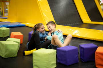 Happy smiling 11 years old kids jumping on trampoline indoors in entertainment center. Active children leisure, jumping and playing on trampoline in sport center. Amusement park. Sport activity