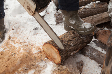 A man is sawing a log with a chainsaw in the snow in winter. Outdoor concept.