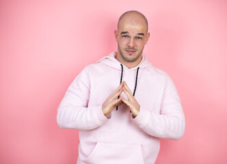 Wall Mural - Young bald man wearing casual sweatshirt over pink isolated background with Hands together and fingers crossed smiling relaxed and cheerful. Success and optimistic