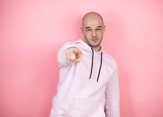 Wall Mural - Young bald man wearing casual sweatshirt over pink isolated background pointing to the front with finger