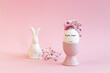 Easter egg with a black marker drawn face in a pink vase with flowers and bunny on pink .